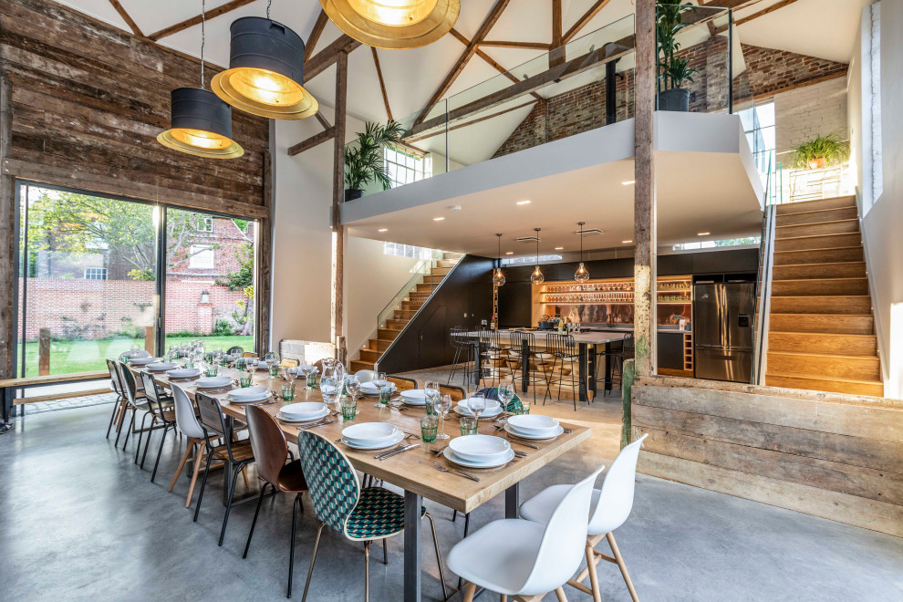 Photo of an expansive industrial open plan dining in Hertfordshire with white walls, brown floor, exposed beam and brick walls.
