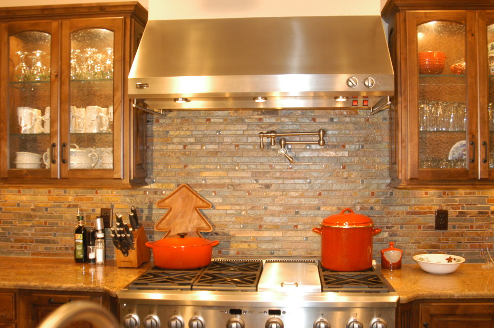 Photo of a large country l-shaped eat-in kitchen in Denver with raised-panel cabinets, dark wood cabinets, granite benchtops, multi-coloured splashback, stone tile splashback, stainless steel appliances, with island and brown benchtop.