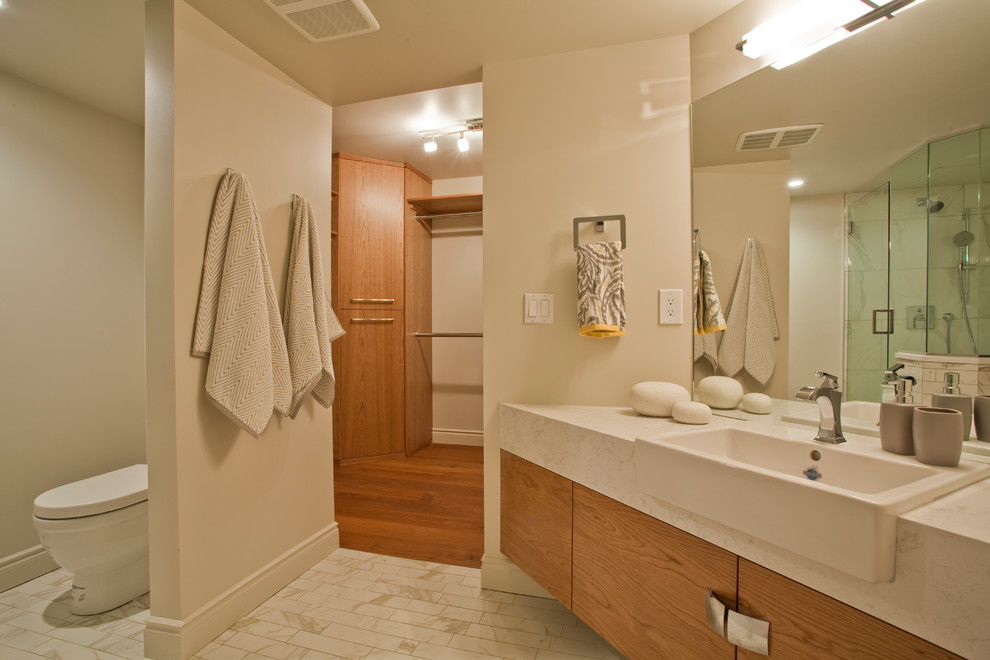 This is an example of a mid-sized modern master bathroom in Edmonton with flat-panel cabinets, medium wood cabinets, a freestanding tub, a curbless shower, a one-piece toilet, white tile, white walls, porcelain floors, a vessel sink, engineered quartz benchtops, grey floor, a hinged shower door and grey benchtops.