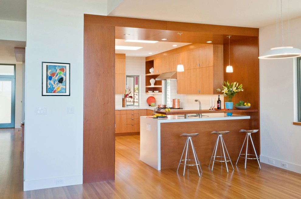 This is an example of a mid-sized transitional u-shaped eat-in kitchen in San Francisco with flat-panel cabinets, medium wood cabinets, quartz benchtops, glass tile splashback, medium hardwood floors, a double-bowl sink, white splashback, stainless steel appliances and no island.