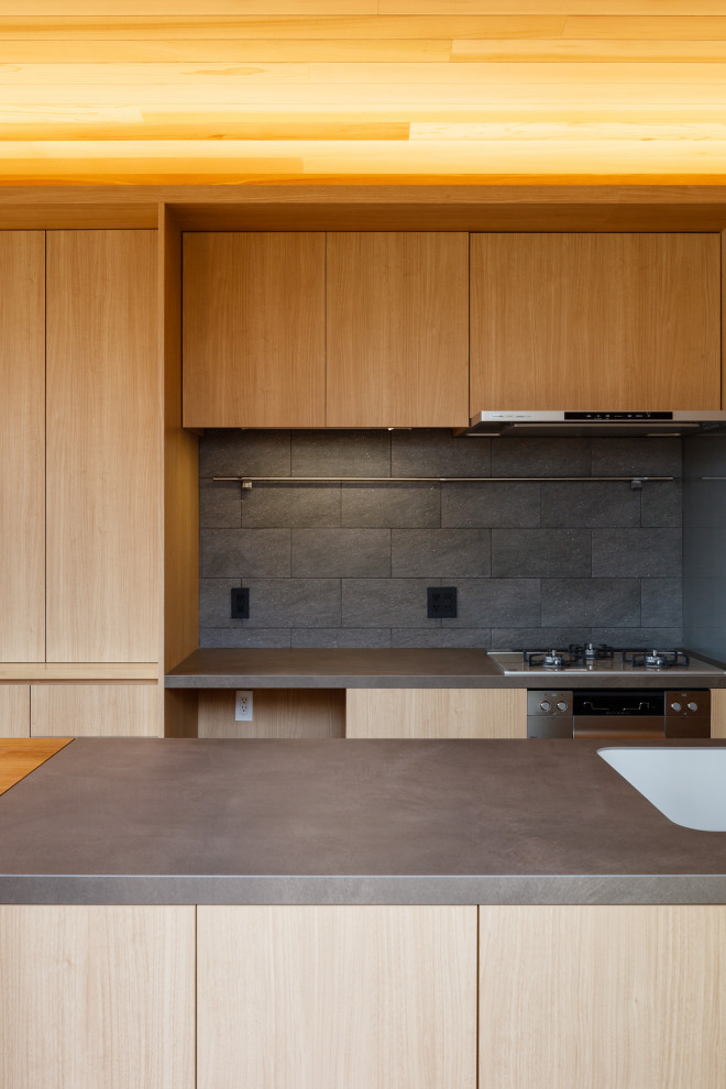 Scandinavian galley open plan kitchen in Tokyo with an undermount sink, flat-panel cabinets, light wood cabinets, tile benchtops, grey splashback, ceramic splashback, stainless steel appliances, with island, grey benchtop and wood.