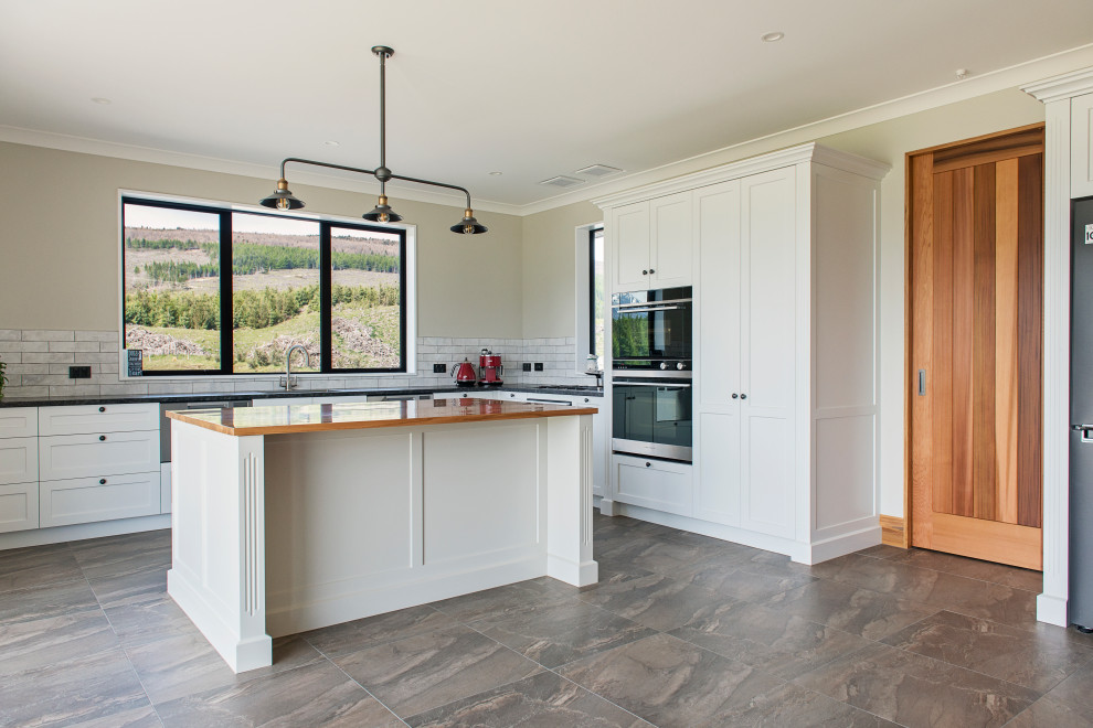 This is an example of a country kitchen/diner with recessed-panel cabinets, grey cabinets, grey splashback, ceramic splashback, ceramic flooring, an island and brown floors.