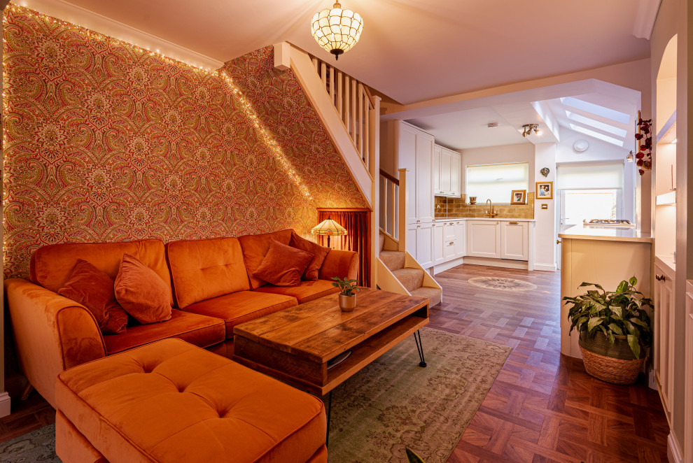На фото: открытая гостиная комната среднего размера:: освещение в стиле фьюжн с оранжевыми стенами, полом из ламината, мультимедийным центром, коричневым полом, потолком с обоями и обоями на стенах с