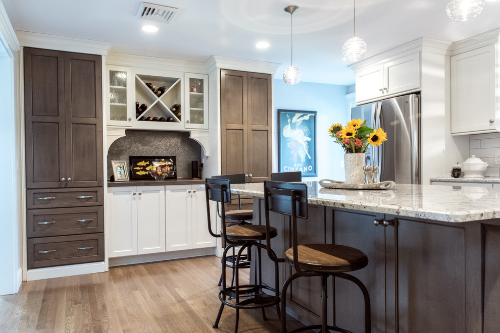 Inspiration for a mid-sized transitional u-shaped medium tone wood floor enclosed kitchen remodel in Providence with a double-bowl sink, white cabinets, granite countertops, white backsplash, subway tile backsplash, stainless steel appliances, an island and recessed-panel cabinets