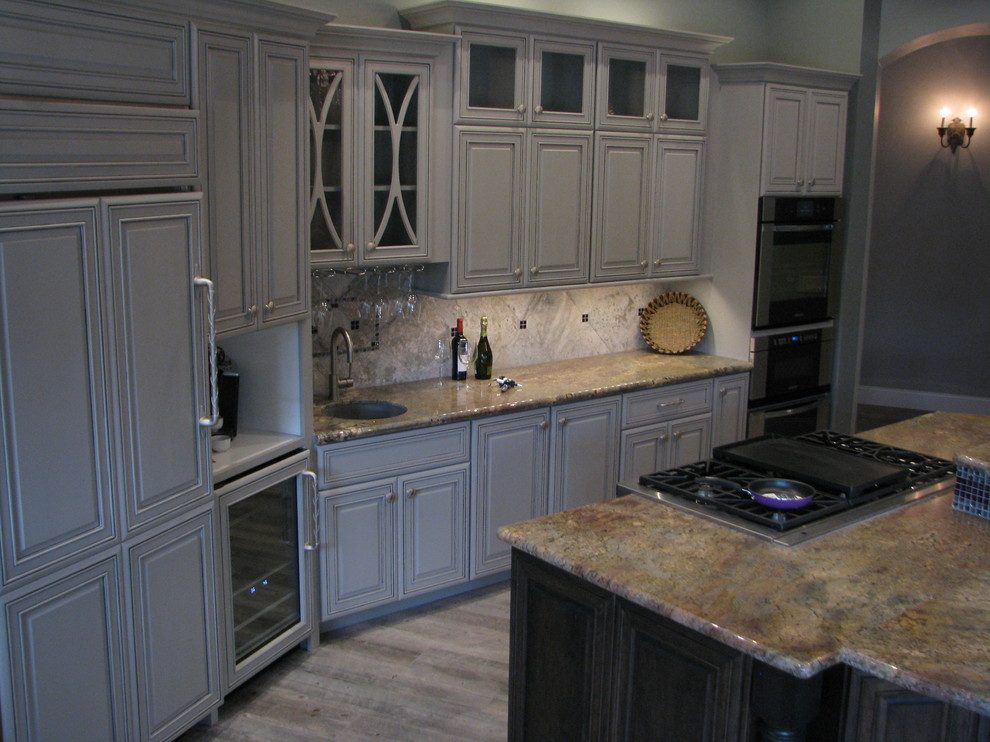 Example of a huge transitional l-shaped porcelain tile open concept kitchen design in Phoenix with an undermount sink, raised-panel cabinets, gray cabinets, granite countertops, gray backsplash, stone tile backsplash, stainless steel appliances and an island