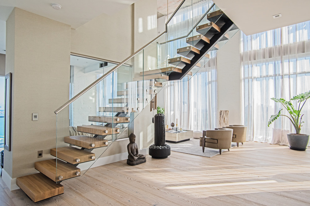 Large modern wood l-shaped staircase in Tampa with open risers and glass railing.