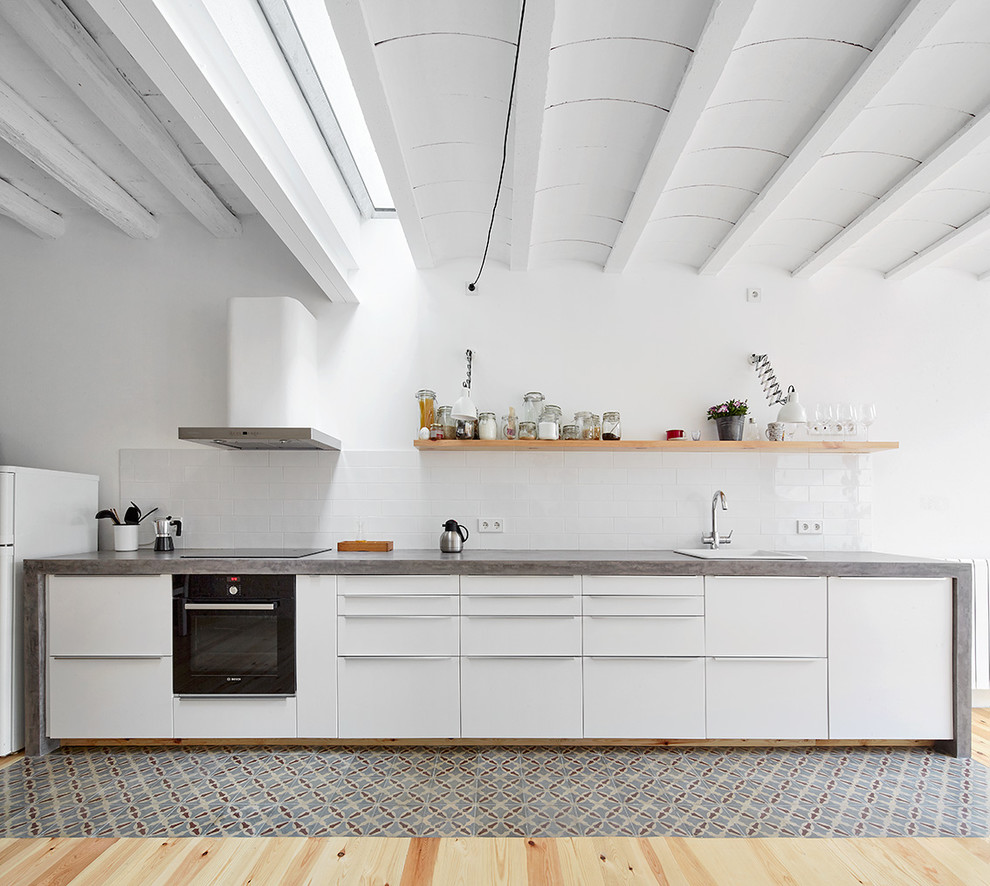 Inspiration for a mid-sized scandinavian single-wall open plan kitchen in Other with a drop-in sink, flat-panel cabinets, white cabinets, concrete benchtops, white splashback, subway tile splashback, light hardwood floors, black appliances and no island.