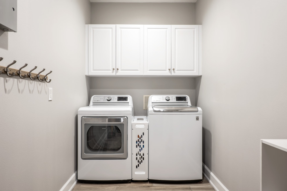 Inspiration for a large traditional single-wall utility room in Tampa with raised-panel cabinets, white cabinets, beige walls, porcelain floors, a side-by-side washer and dryer and grey floor.