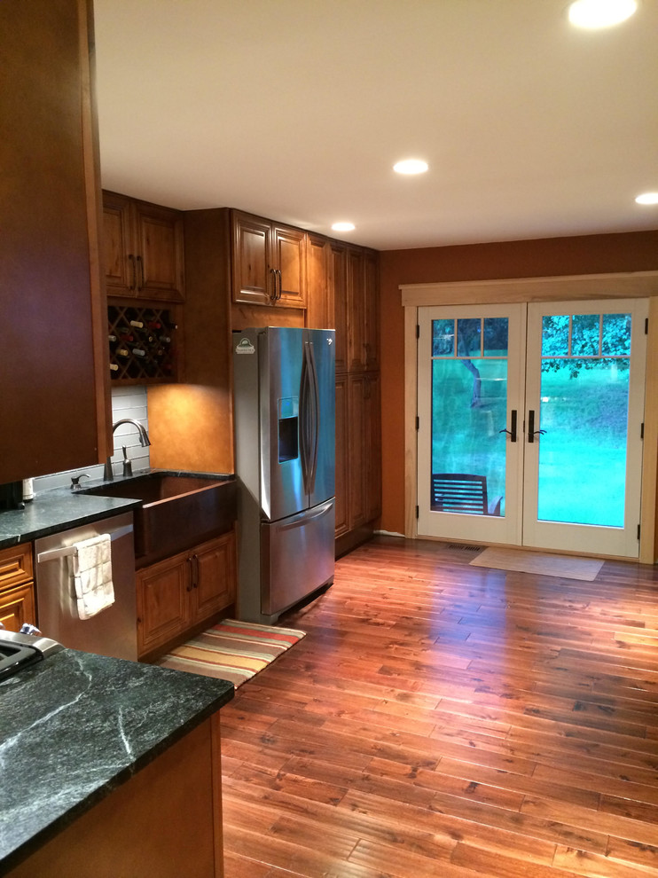 Inspiration for a large rustic l-shaped medium tone wood floor eat-in kitchen remodel in St Louis with a farmhouse sink, raised-panel cabinets, granite countertops, gray backsplash, glass tile backsplash, stainless steel appliances and a peninsula