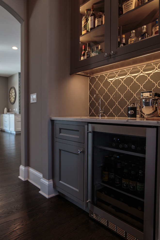 Large transitional single-wall wet bar in Chicago with an undermount sink, shaker cabinets, grey cabinets, marble benchtops, grey splashback, glass tile splashback and dark hardwood floors.