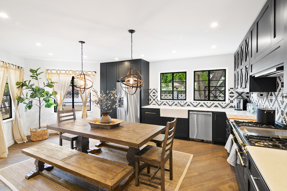 Transitional l-shaped medium tone wood floor and brown floor eat-in kitchen photo in Los Angeles with a farmhouse sink, shaker cabinets, black cabinets, multicolored backsplash, stainless steel appliances, no island and beige countertops