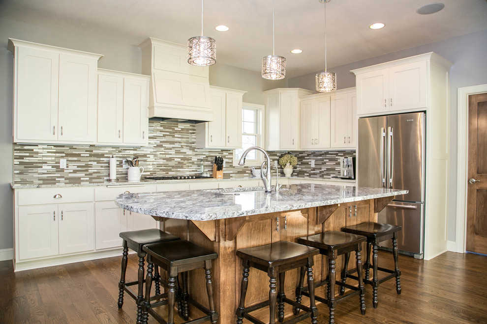 Example of a transitional u-shaped medium tone wood floor open concept kitchen design in Minneapolis with an undermount sink, shaker cabinets, white cabinets, granite countertops, multicolored backsplash, ceramic backsplash, stainless steel appliances and an island