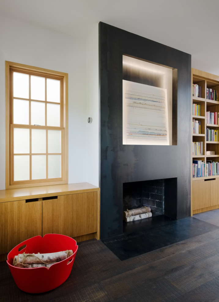 Photo of a large modern home office in Sacramento with a library, white walls, dark hardwood floors, a standard fireplace, a concrete fireplace surround and black floor.