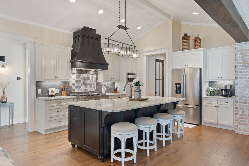 Photo of a large farmhouse l-shaped kitchen/diner in Other with a belfast sink, shaker cabinets, white cabinets, engineered stone countertops, black splashback, marble splashback, stainless steel appliances, medium hardwood flooring, an island, beige floors, white worktops and a timber clad ceiling.