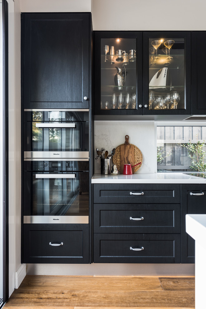 This is an example of a mid-sized transitional u-shaped eat-in kitchen in Melbourne with a double-bowl sink, shaker cabinets, black cabinets, quartz benchtops, medium hardwood floors, no island and white benchtop.