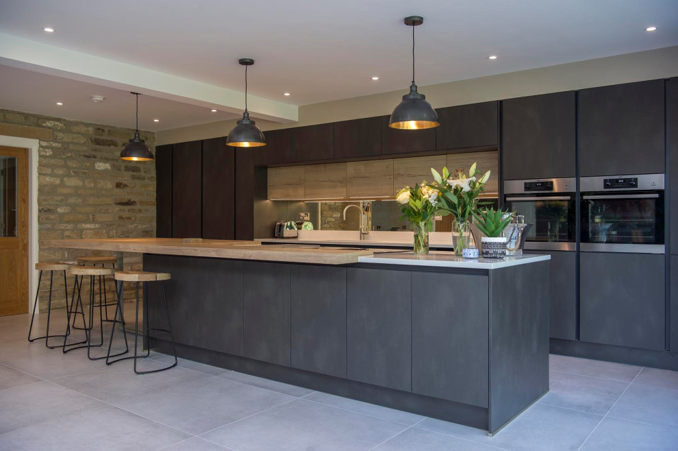 Inspiration for a mid-sized contemporary galley kitchen in Other with flat-panel cabinets, light wood cabinets, ceramic floors, with island, grey floor, an undermount sink, mirror splashback, stainless steel appliances and grey benchtop.