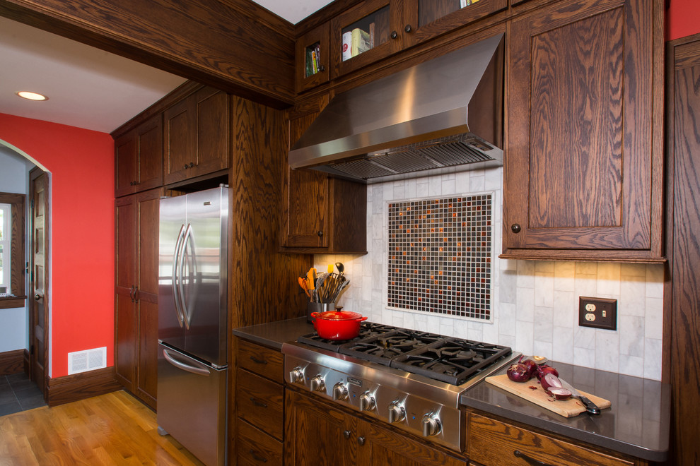 Enclosed kitchen - small craftsman u-shaped medium tone wood floor enclosed kitchen idea in Columbus with recessed-panel cabinets, dark wood cabinets, quartz countertops, gray backsplash, stone tile backsplash, stainless steel appliances and red walls