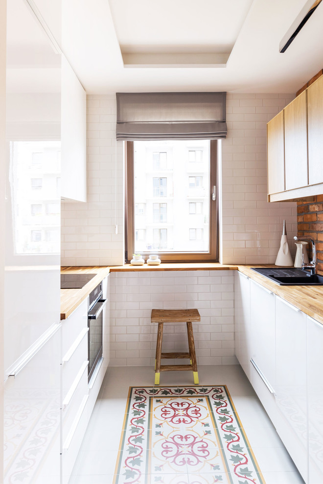 Photo of a small scandinavian galley kitchen in Other with flat-panel cabinets, white cabinets, wood benchtops, white splashback, subway tile splashback, stainless steel appliances and no island.