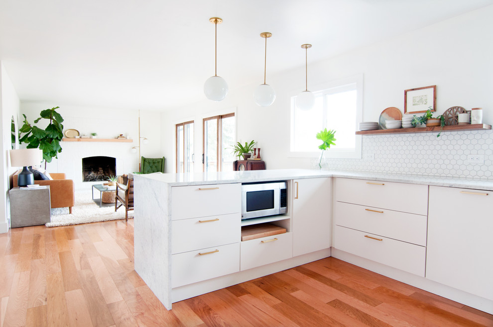 This is an example of a mid-sized midcentury u-shaped open plan kitchen in Denver with a single-bowl sink, flat-panel cabinets, white cabinets, marble benchtops, white splashback, porcelain splashback, stainless steel appliances, light hardwood floors and a peninsula.