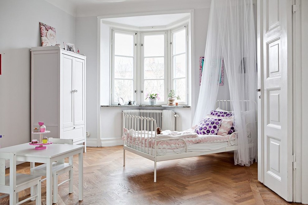 This is an example of a mid-sized scandinavian gender-neutral kids' bedroom for kids 4-10 years old in Malmo with white walls and medium hardwood floors.
