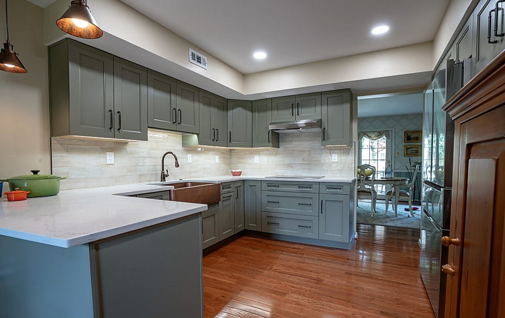 Example of a mid-sized classic u-shaped medium tone wood floor enclosed kitchen design in Other with a farmhouse sink, recessed-panel cabinets, green cabinets, quartz countertops, white backsplash, ceramic backsplash, stainless steel appliances and white countertops