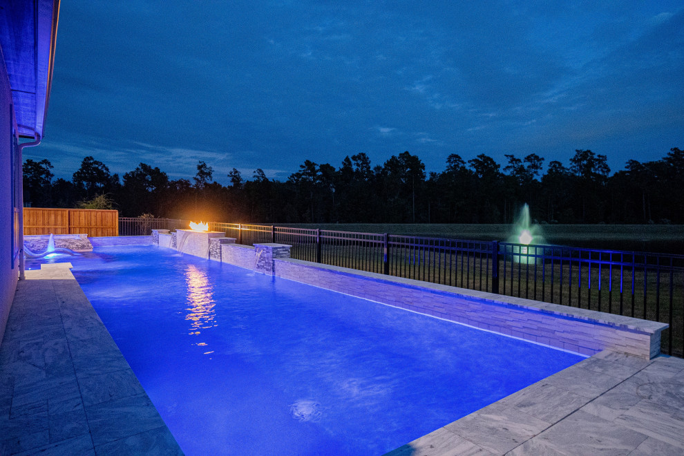 Large modern back rectangular swimming pool in Houston with natural stone paving.