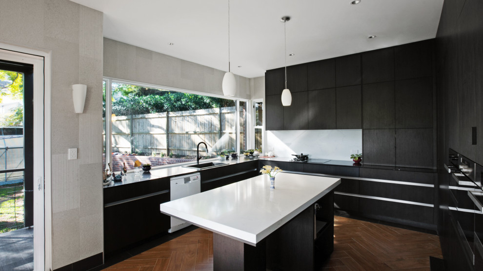 Photo of a large modern u-shaped open plan kitchen in Sydney with with island, a drop-in sink, flat-panel cabinets, black cabinets, limestone benchtops, white splashback, limestone splashback, stainless steel appliances, ceramic floors, beige floor and white benchtop.
