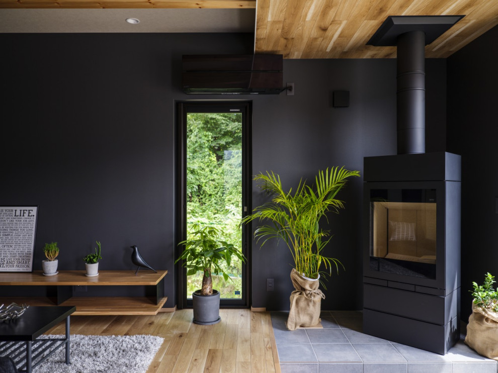 This is an example of a mid-sized modern open concept living room in Other with black walls, light hardwood floors, a wood stove, a tile fireplace surround, a freestanding tv, brown floor, wallpaper and wallpaper.