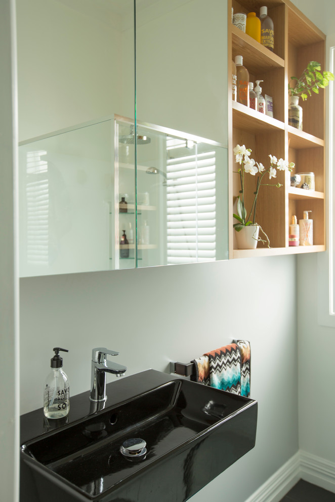 This is an example of a small modern master bathroom in Auckland with glass-front cabinets, light wood cabinets, a corner shower, ceramic floors, a wall-mount sink and grey floor.