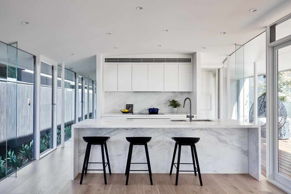 Contemporary galley kitchen in Melbourne with an undermount sink, flat-panel cabinets, white cabinets, medium hardwood floors, with island, brown floor and white benchtop.
