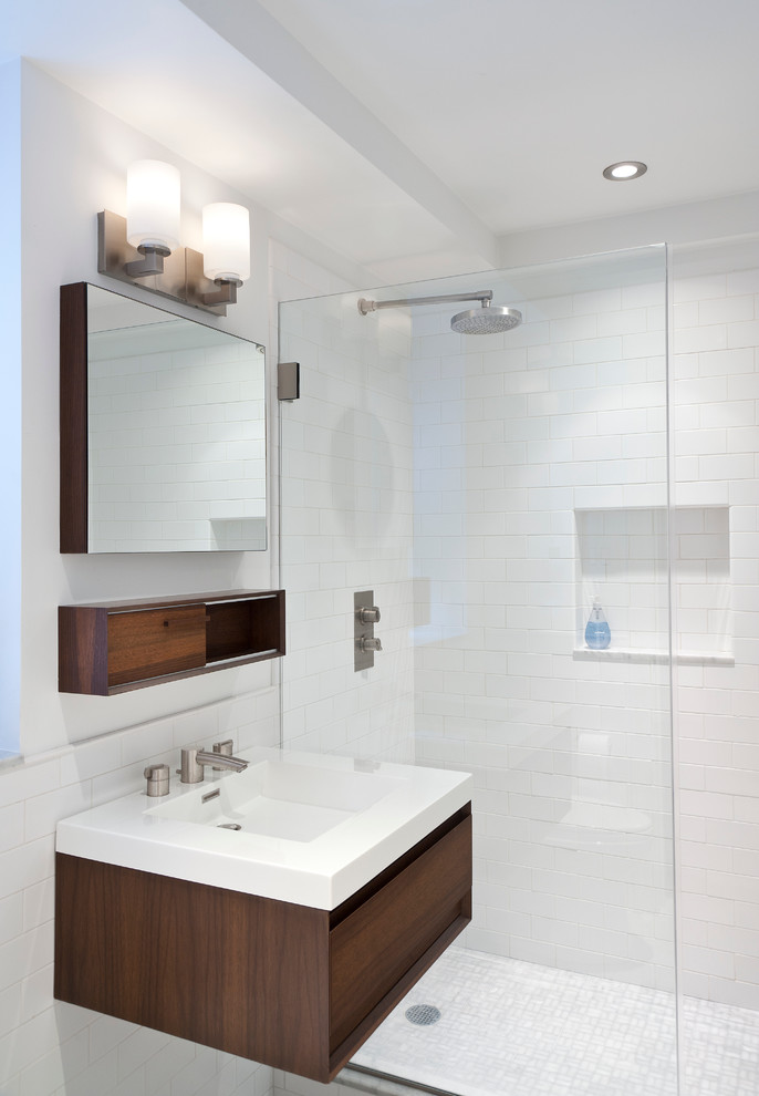 Inspiration for a small modern master bathroom in New York with an integrated sink, flat-panel cabinets, dark wood cabinets, solid surface benchtops, an alcove shower, white tile, subway tile, white walls, marble floors, a sliding shower screen and grey floor.