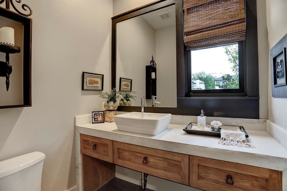 This is an example of a mid-sized traditional powder room in Houston with medium wood cabinets, a two-piece toilet, a vessel sink, grey floor, white benchtops, recessed-panel cabinets, beige walls, porcelain floors and marble benchtops.