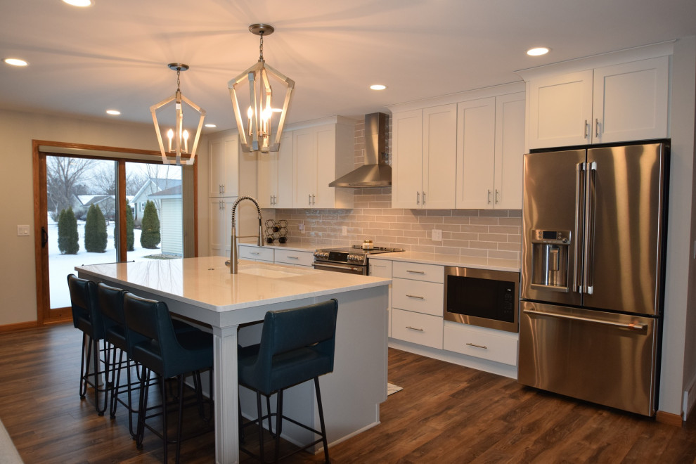 Inspiration for a transitional galley vinyl floor and brown floor kitchen remodel with an undermount sink, shaker cabinets, white cabinets, quartz countertops, beige backsplash, subway tile backsplash, stainless steel appliances, an island and white countertops