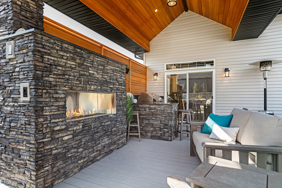 This is an example of a mid-sized country backyard and ground level deck in Edmonton with with fireplace, a roof extension and glass railing.