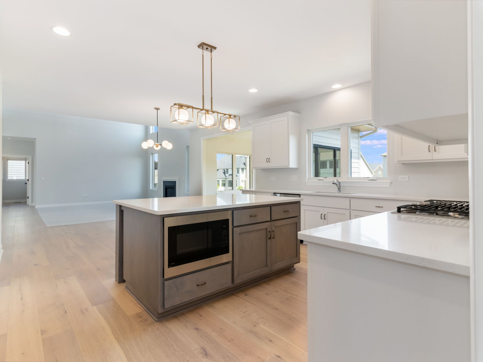 This is an example of a mid-sized contemporary kitchen in Chicago with white cabinets, white splashback, stainless steel appliances, with island, brown floor and white benchtop.