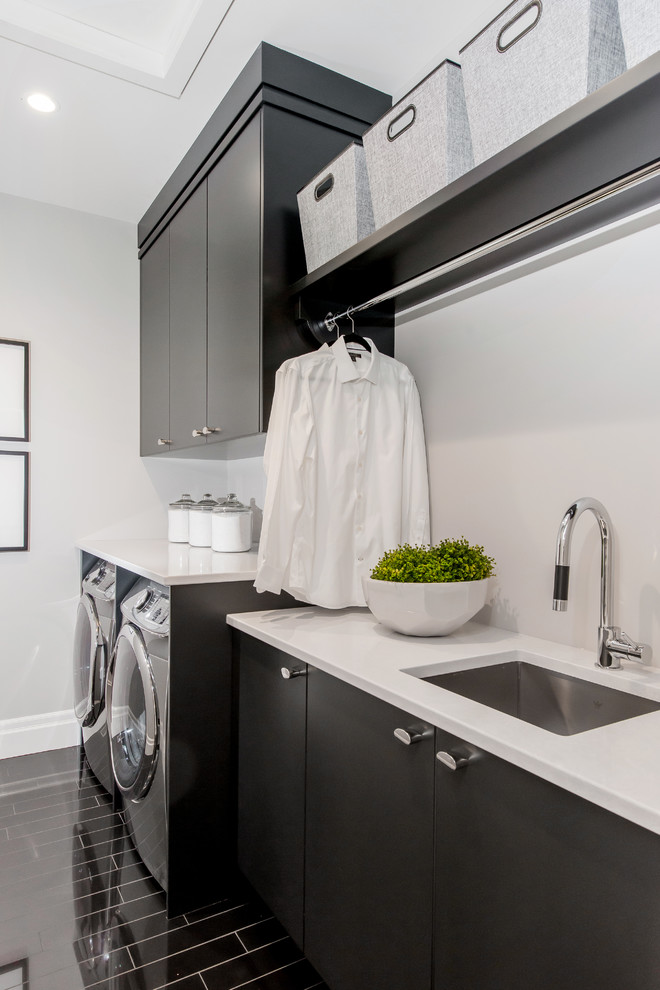 Example of a large transitional single-wall ceramic tile dedicated laundry room design in Calgary with an undermount sink, flat-panel cabinets, gray cabinets, quartz countertops, gray walls, a side-by-side washer/dryer and white countertops
