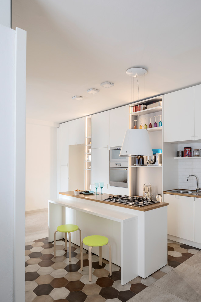 Design ideas for a contemporary galley separate kitchen in Milan with a double-bowl sink, flat-panel cabinets, white cabinets, wood benchtops, white splashback, stainless steel appliances, with island, subway tile splashback, multi-coloured floor and brown benchtop.