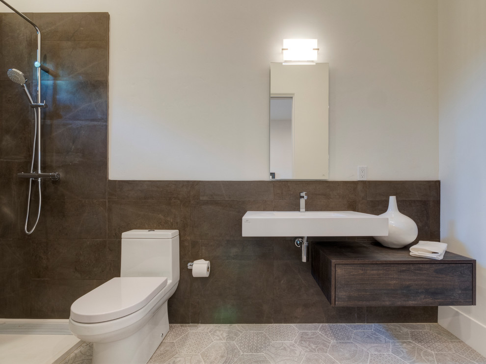 This is an example of a mid-sized bathroom in San Francisco with an open shower, a one-piece toilet, brown tile, stone tile, white walls, a wall-mount sink and solid surface benchtops.