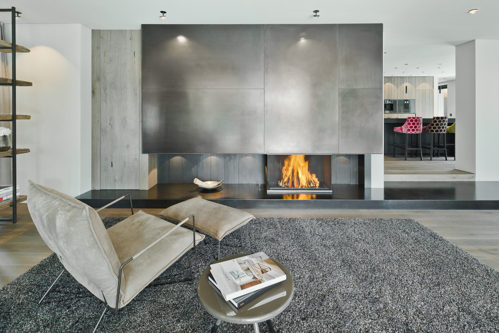 Design ideas for an expansive contemporary open concept family room in Munich with white walls, medium hardwood floors, a wood stove, a metal fireplace surround, brown floor and a concealed tv.