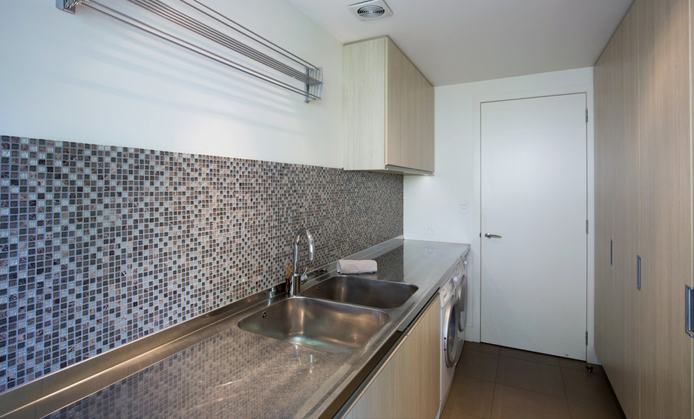 Photo of a large modern single-wall dedicated laundry room in Auckland with a double-bowl sink, flat-panel cabinets, medium wood cabinets, stainless steel benchtops, white walls, ceramic floors and a side-by-side washer and dryer.