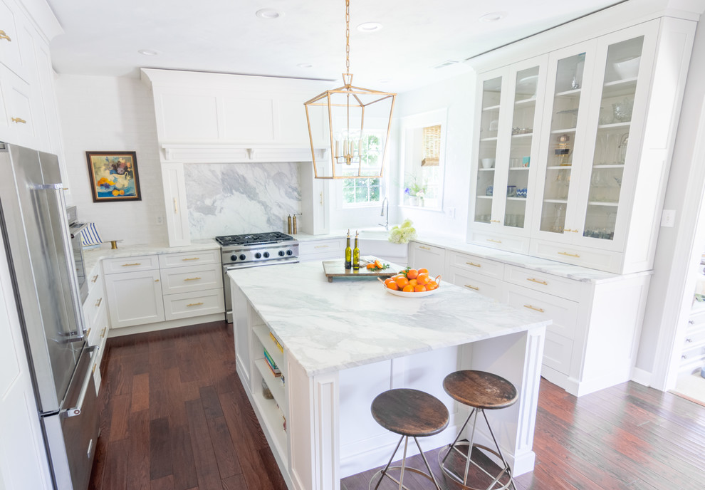Transitional u-shaped dark wood floor and brown floor kitchen photo with a farmhouse sink, shaker cabinets, white cabinets, marble countertops, marble backsplash, stainless steel appliances and an island