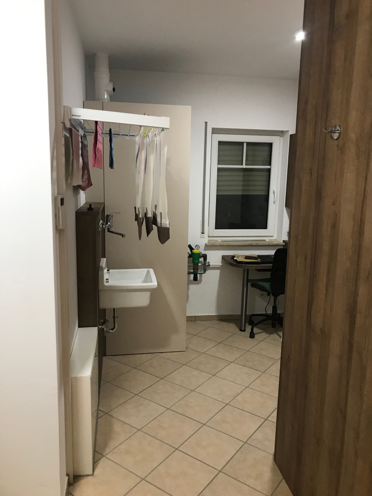 Multifunktionaler, Mittelgroßer Moderner Hauswirtschaftsraum mit Ausgussbecken, flächenbündigen Schrankfronten, beigen Schränken, Laminat-Arbeitsplatte, weißer Wandfarbe, Keramikboden, Waschmaschine und Trockner gestapelt, beigem Boden und brauner Arbeitsplatte in Berlin