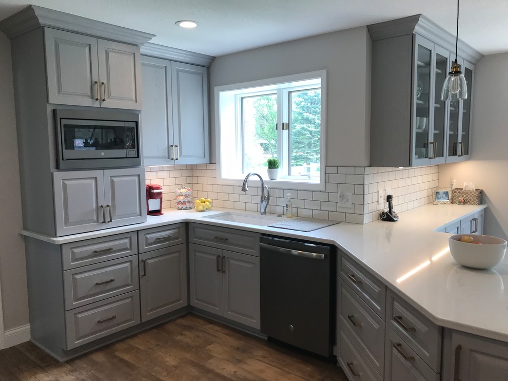 Example of a mid-sized transitional u-shaped vinyl floor and brown floor enclosed kitchen design with an undermount sink, raised-panel cabinets, gray cabinets, quartz countertops, white backsplash, ceramic backsplash, a peninsula and white countertops