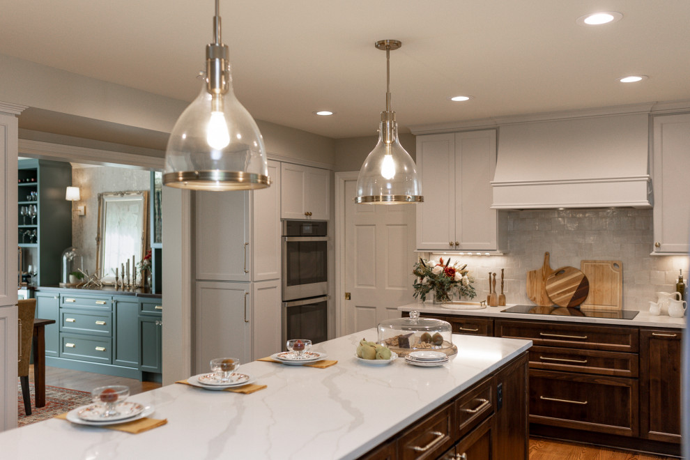 Example of a mid-sized transitional l-shaped medium tone wood floor and brown floor eat-in kitchen design with an undermount sink, medium tone wood cabinets, quartz countertops, beige backsplash, terra-cotta backsplash, stainless steel appliances, an island, white countertops and recessed-panel cabinets