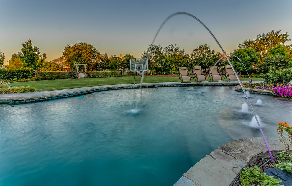 Inspiration for a large tropical backyard custom-shaped natural pool in Dallas with a water feature and stamped concrete.