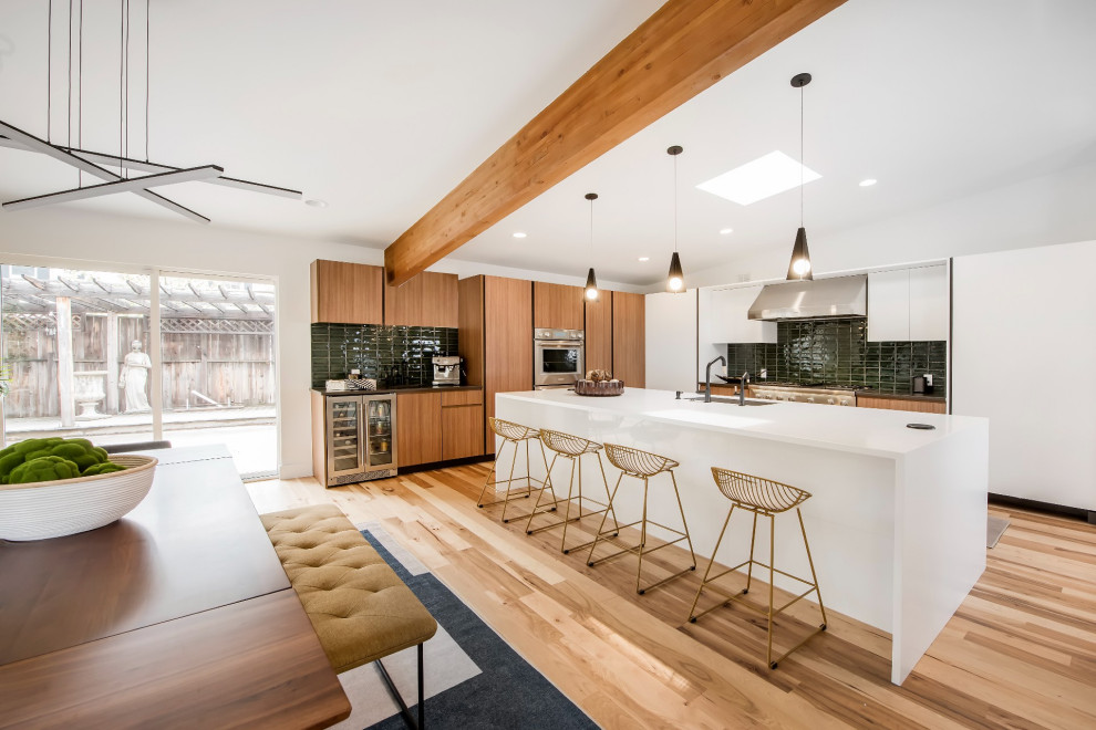 Inspiration for a large midcentury l-shaped open plan kitchen in Denver with an undermount sink, brown cabinets, green splashback, subway tile splashback, stainless steel appliances, light hardwood floors, with island, brown floor and white benchtop.