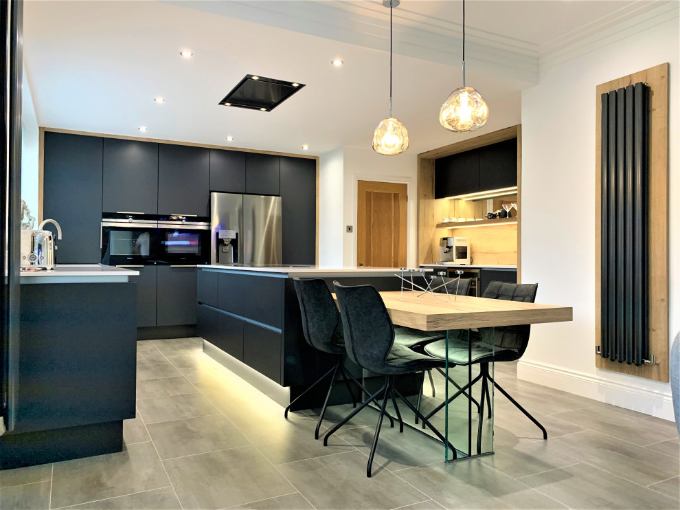 This is an example of a mid-sized contemporary u-shaped open plan kitchen in Other with a single-bowl sink, flat-panel cabinets, medium wood cabinets, solid surface benchtops, black appliances, vinyl floors, with island and white benchtop.