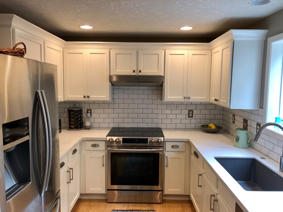This is an example of a small traditional u-shaped separate kitchen in Portland with an undermount sink, recessed-panel cabinets, white cabinets, quartz benchtops, subway tile splashback, stainless steel appliances, light hardwood floors, no island, yellow floor and white benchtop.