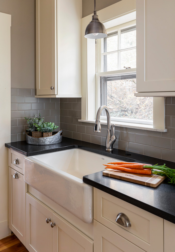 Example of a mid-sized transitional galley light wood floor kitchen pantry design in Boston with a farmhouse sink, shaker cabinets, white cabinets, granite countertops, gray backsplash, subway tile backsplash, stainless steel appliances, no island and black countertops