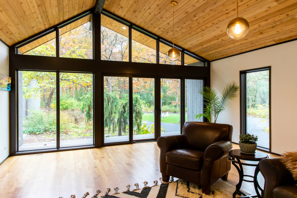 This is an example of a large midcentury enclosed family room in Chicago with white walls, light hardwood floors, a two-sided fireplace, a plaster fireplace surround, a concealed tv, brown floor and vaulted.